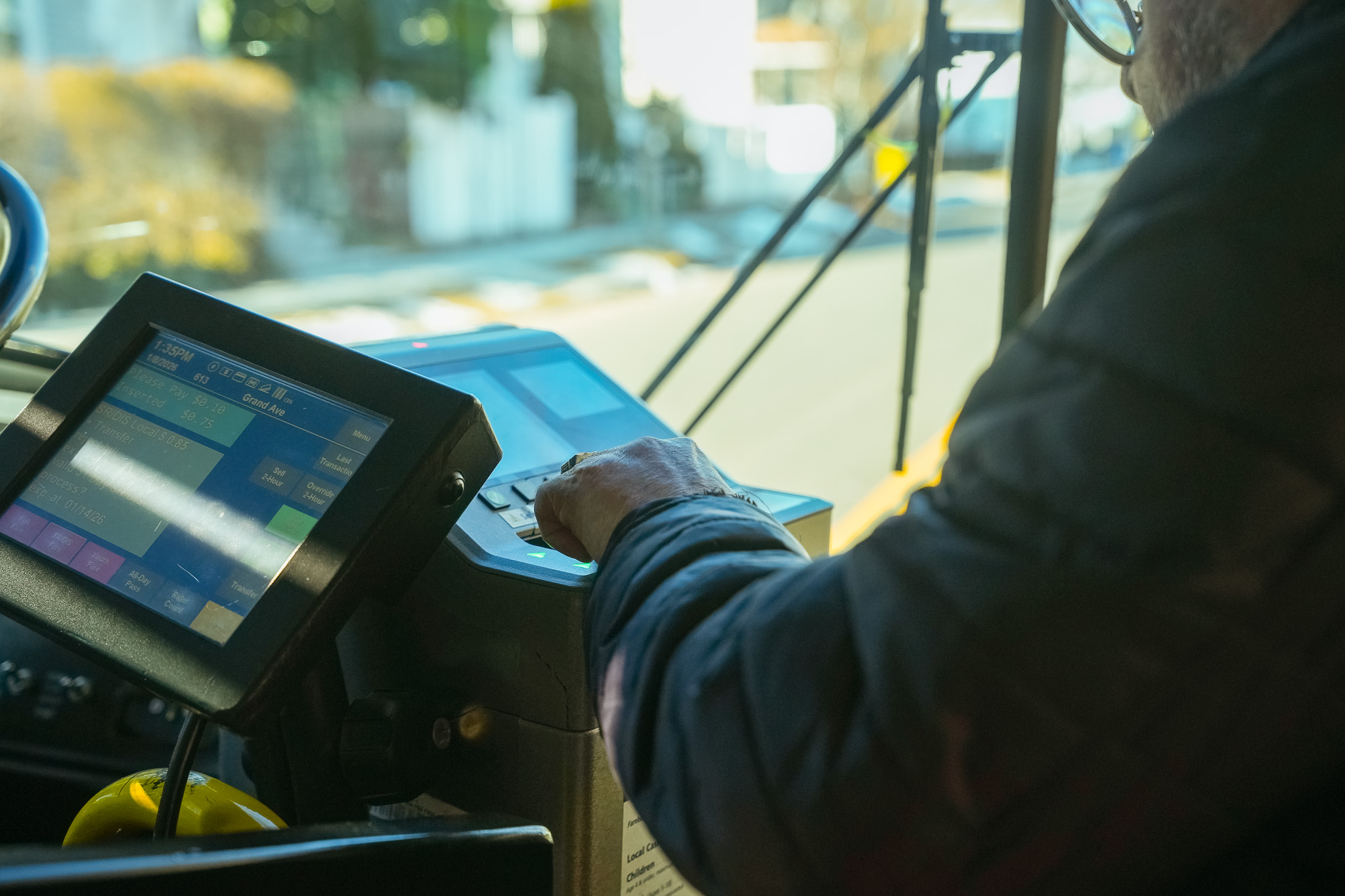 Close-up of a bus driver using a fare collection device with a screen displaying fare information and buttons for transactions.
